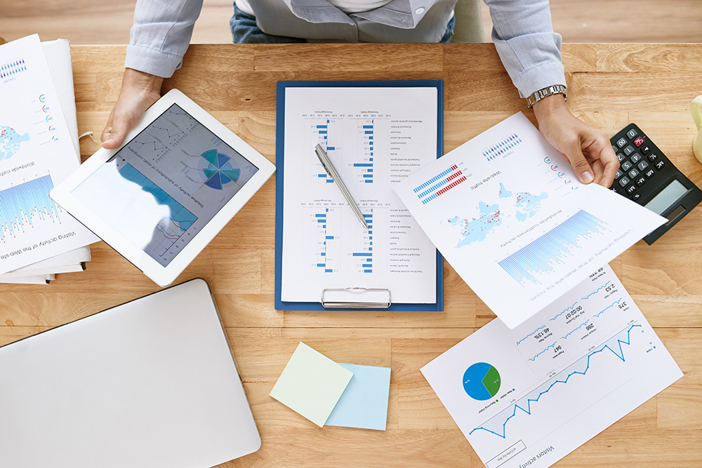 Overhead view of a desk with various charts and graphs printed and on a tablet